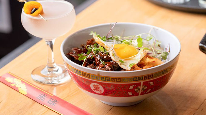 A bulgogi beef and rice bowl served alongside a cocktail